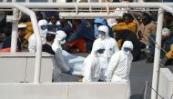 (FILES) This file photo taken on April 20, 2015 shows rescued migrants watching as the body of a person who died after a fishing boat carrying migrants capsized off the Libyan coast, is brought ashore along with 23 others retreived by the Italian Coast Gu