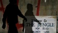 The shadow of a migrant falls on a sign with the population of 