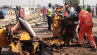 Emergency personnel stand near the wreacked remains of a vehicle ripped apart following two suicide bombings in Nigeria's northeast city of Maiduguri on October 29, 2016 where at least nine people and scores of others were injured. / AFP / JOSHOUA OMIRIN