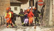 Firefighters and rescuers carry a woman on a wheelchair after a 6.6 magnitude earthquake on October 30, 2016 in Norcia. / AFP / Fabrizio Troccoli.