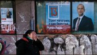 A street vendor hides her face as she sells clothes in front of electoral posters of former Bulgarian airforce chief Rumen Radev, candidate of the opposition Socialists, in Sofia on November 11, 2016. AFP / DIMITAR DILKOFF