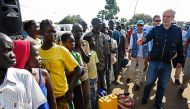 EU Commissioner for Humanitarian and Crisis Management, Christos Stylianides speaks with newly arrived refugees from South Sudan as they queue in line waiting to be registered on November 11, 2016 at Kuluba Reception Centre in Koboko District, North of th