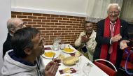 Father Angel Garcia Rodriguez (R) claps beside homeless people eating a free dinner at the Robin Hood restaurant in Madrid on December 1, 2016. AFP / GERARD JULIEN
