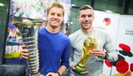 Formula One World Champion Nico Rosberg (left) raises the trophy next to former German player Lukas Podolski with the football World Cup trophy in Cologne, Germany on Wednesday.