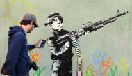 (FILES) This file photo taken on February 17, 2011 shows a graffito attributed to secretive British artist Banksy, depicting a child wielding a machine gun, in black and white, surrounded by colored flowers, in Westwood, California. AFP / GABRIEL BOUYS