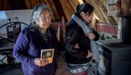 Holding a copy of her book, Cristina Calderon (L), 89, the last native speaker of the Yagan language, walks with her granddaughter Claudia Gonzalez in the local community center in Puerto Williams, southern Chile, on April 23, 2017. AFP / Martin BERNETTI
