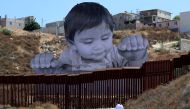 A small boy walks with his mother in front of French artist JR's image of an inquisitive baby looking into the United States over the U.S.- Mexico border wall towards Tecate, California, U.S., September 15, 2017. REUTERS/Mike Blake 
