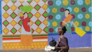 This photo taken on November 9, 2017 shows a fisherwoman walking past a wall painting of the St+art Festival at Sassoon Dock, one of the oldest fishing docks in Mumbai. AFP / INDRANIL MUKHERJEE 