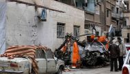 Syrians look at damaged vehicles in a street that was reportedly struck by mortar shrapnel from rebel bombardment the previous day in Jaramana, southeast of the Syrian capital Damascus, on February 12, 2018. / AFP / LOUAI BESHARA
