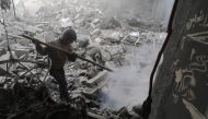 A Syrian boy puts off a fire amid destroyed buildings following government air strikes in the Eastern Ghouta rebel-held enclave of Douma, on the outskirts of the capital Damascus on March 19, 2018.   AFP / HAMZA AL-AJWEH
