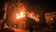 TOPSHOT - A picture taken early on March 23, 2018 shows a man standing looking at flames erupting in a building following regime bombardment in Douma, one of the few remaining rebel-held pockets in Eastern Ghouta on the outskirts of the capital Damascus. 