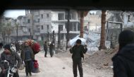 Syrian people carry their belongings as they walk down a destroyed street as they prepare to evacuate one of the few remaining rebel-held pockets in Arbin, in Eastern Ghouta, on the outskirts of the Syrian capital Damascus, on March 24, 2018.  AFP / ABDUL