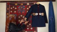 An Afghan tailor hanging an embroidered coat on the wall at Zarif Design House in Kabul. AFP / WAKIL KOHSAR 
 