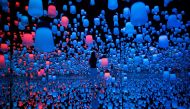 In this picture taken on May 1, 2018 a Japanese member of Teamlab collective walks and poses in a digital installation room with hanging lamps, that illuminate as the visitor nears and the light moving from one lamp to another around the room, at Mori Bui