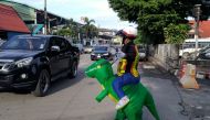 Thai police sargent Tanit Bussabong directs traffic wearing a costume where he appears to ride a T-rex dinosaur outside a school in Nakhon Nayok on June 4, 2018. AFP / Stephen J. BOITANO
 