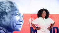 US TV personality Oprah Winfrey poses on the red carpet next to a banner depecting late former South African president Nelson Mandela, as she arrives to attend an event to mark 100 years since the birth of Nelson Mandela, at the University of Johannesburg