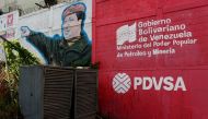 The logo of the Venezuelan state oil company PDVSA is seen next to a mural depicting late President Hugo Chavez at a gas station in Caracas, March 2, 2017. Reuters/Carlos Garcia Rawlins