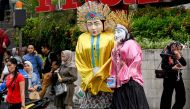 This picture taken on April 26, 2019 shows people walking past Ondel-ondel effigies worn by children busking for money on a street in Jakarta.  AFP / Goh Chai Hin 