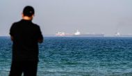 A man stands along a beach as tanker ships are seen in the waters of the Gulf of Oman off the coast of the eastern UAE emirate of Fujairah on June 15, 2019. / AFP / GIUSEPPE CACACE