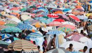 Moroccans walk between parasols at the beach in the Moroccan capital Rabat on August 21, 2016. AFP/ Fadel Senna