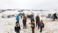 Internally displaced children stand in snow near tents at an informal displacement camp in Azaz