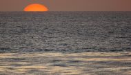 The sun sets as a fisherman casts his line in the Pacific Ocean while sitting on a surfboard off the coast of Cardiff, California April 1, 2008. REUTERS/Mike Blake/File Photo