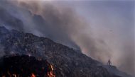 A person picks through trash for reusable items as a fire rages at the Bhalswa landfill in New Delhi on April 27, 2022. (Image credit: Manish Swarup via AP)