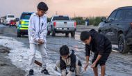 Children toss handfuls of hail particles picked up off the side of a road after a storm in the Umm al-Haiman district, on December 27, 2022. (Photo by Yasser Al-Zayyat / AFP)