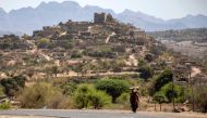 A woman carrying tree branches to be used as firewood walks along a road, on the outskirts of Taez, in Yemen, on February 24, 2023. (Photo by AHMAD AL-BASHA / AFP)