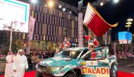 Nasser Saleh Al Attiyah waves Qatar's flag as QMMF President Abdulrahman Al Mannai walks on during the ceremonial start at Lusail Boulevard, yesterday.  