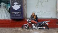 A man sits by his motorcycle on a shop's stairs as water floods a street amid heavy rainfall in Sanaa, Yemen, on March 31, 2023. (Photo by Mohammed Huwais / AFP)