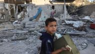 A Palestinian boy salvages belongings from a destroyed home following Israeli bombardment in Rafah in the southern Gaza Strip, on October 18, 2023. (Photo by Said Khatib / AFP)