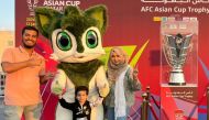 A family of three pose for a photograph alongside the AFC Asian Cup champions trophy and Zkriti, one of the mascots.