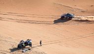 Nasser Racing’s Qatari driver Nasser Al Attiyah waves to Team Audi Sport’s Spanish driver Carlos Sainz as he stands by his car following a mechanical failure in the dunes yesterday. AFP