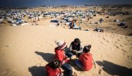 Displaced Palestinian children play on a sand dune above a makeshift camp on the Egyptian border, west of Rafah in the southern Gaza Strip on January 14, 2024. Photo by AFP