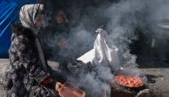 A displaced Palestinian woman uses a makeshift stove to cook a meal on the street in Rafah in the southern Gaza Strip on February 11, 2024, amid the ongoing conflict between Israel and the Palestinian militant group Hamas. (Photo by Mohammed Abed / AFP)