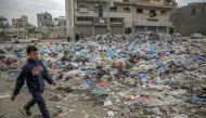 A Palestinian boy walks along a street dumped with garbage in Gaza City on February 24, 2024. Photo by AFP