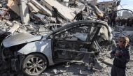 A young Palestinian boy stands next to a wrecked car in the rubble of a residential building hit in an overnight Israeli air strike in Rafah in the southern Gaza Strip on March 9, 2023, amid continuing battles between Israel and the Palestinian militant group Hamas. (Photo by SAID KHATIB / AFP)
