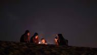 People sit by the fire at a camp for displaced Palestinians in Rafah, in the southern Gaza Strip, on the eve of the holy month of Ramadan on March 10, 2024. Photo by MOHAMMED ABED / AFP