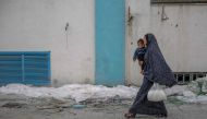 A woman carries her child and a bag of flour after humanitarian aid was distributed in Gaza City on March 17, 2024, amid ongoing battles between Israel and the Palestinian group Hamas. (Photo by AFP)
