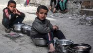 Boys sit with empty pots as displaced Palestinians queue for meals provided by a charity organisation ahead of the fast-breaking 