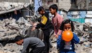 A girl blows a balloon as behind her boys search through the rubble of a destroyed building in Rafah in the southern Gaza Strip on April 5, 2024. (Photo by Mohammed Abed / AFP)
 