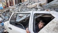 A boy looks out the window from inside a heavily damaged vehicle by the rubble of a collapsed building in Rafah in the southern Gaza Strip on April 9, 2024. (Photo by AFP)
 