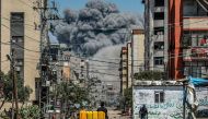 A cloud of smoke erupts down the road from an explosion as a man drives an animal-drawn cart loaded with jerrycans in Nuseirat in the central Gaza Strip on April 17, 2024. (Photo by AFP)