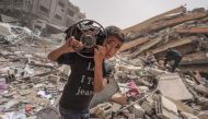 A Palestinian carries a gas cooker as he walks amidst the debris of a destroyed building in the city of Nuseirat in the central Gaza Strip on April 18, 2024.