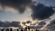 Clouds are pictured behind children at sunset at a camp housing displaced Palestinians in Rafah in the southern Gaza Strip on April 30, 2024. (Photo by AFP)
