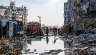 Displaced Palestinians walk around a puddle in front of destroyed buildings and tents in Khan Yunis in the southern Gaza Strip on May 16, 2024. (Photo by AFP)