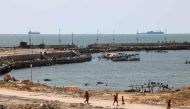 Palestinians walk past a jetty in Gaza City with a view of navy vessels off the coast as part of a humanitarian 