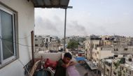 A boy stands on a balcony with a view of billowing smoke due to renewed Israeli strikes in Rafah city in the southern gaza Strip on May 28, 2024. (Photo by Eyad BABA / AFP) 