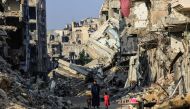 A man with his children walks past destroyed buildings in Khan Yunis on June 20, 2024. (Photo by Eyad Baba / AFP)